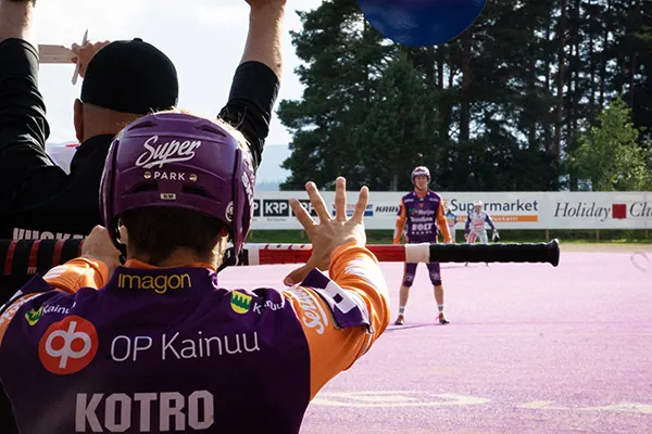 A Sotkamon Jymy player wearing a jersey with the Imagon logo beside a Finnish baseball field.