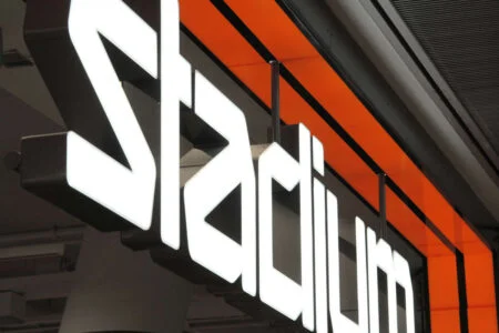 Close-up of white illuminated Stadium letters and an orange facade stripe. Close-up of white illuminated Stadium letters and an orange facade stripe.