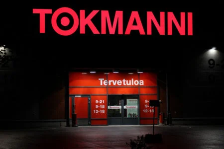 Red illuminated Tokmanni letters above a lit entrance at night. Red illuminated Tokmanni letters above a lit entrance at night.