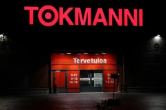 Punaiset Tokmanni-valokirjaimet valaistun sisäänkäynnin yläpuolella pimeässä.