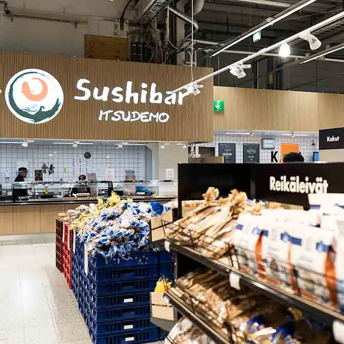 Sushibar Itsudemo logo on a light wood panel behind bread shelves