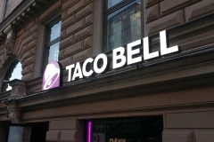 Taco Bellin valkoinen nimiteksti ja violetti kellologo tiilijulkisivussa