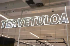 White outline Tervetuloa illuminated letters suspended from a shop ceiling