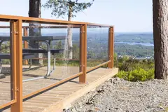 Transparent glass railing on a timber-framed outdoor platform overlooking woodland