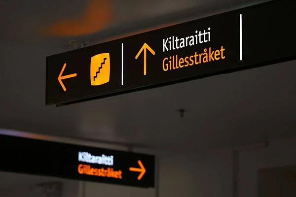 Black illuminated direction signs with orange arrows and the names Kiltaraitti and Gillesstråket