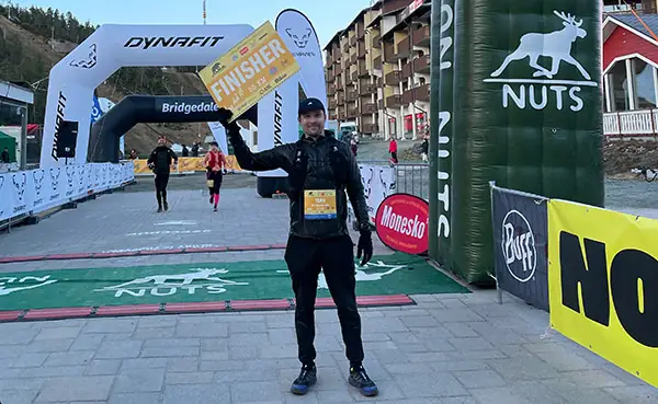 Tero Heikkinen raising his hand beside a branded arch in the finish area of a NUTS event