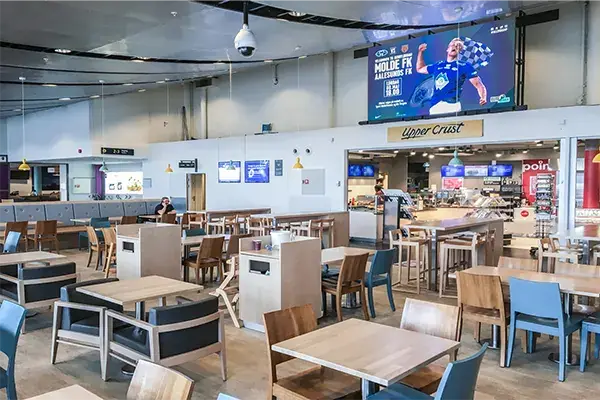Advertising screens on the wall above tables and chairs in the dining area at Molde Airport