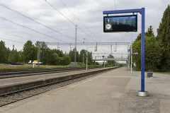 Siniseen pylvääseen kiinnitetty digitaalinen aikataulunäyttö rautatieaseman laiturilla