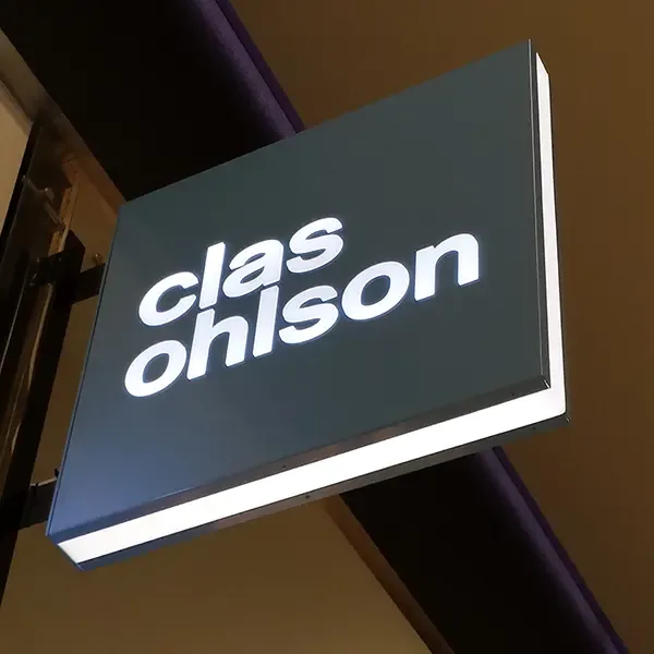 White Clas Ohlson logo on a dark square projecting sign