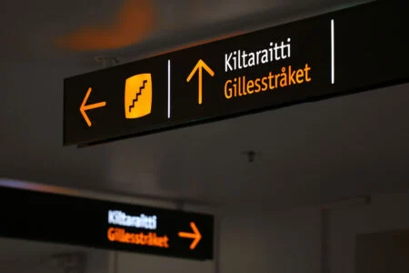 A Kiltaraitti/Gillesstråket sign with illuminated yellow arrows and a stair symbol. A Kiltaraitti/Gillesstråket sign with illuminated yellow arrows and a stair symbol.