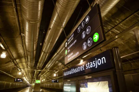 Illuminated direction signs and Nationaltheatret stasjon lettering in a passage leading to an underground station. Illuminated direction signs and Nationaltheatret stasjon lettering in a passage leading to an underground station.
