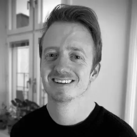 Svartvitt porträtt av Anthony Harvey som ler bredvid ett fönster