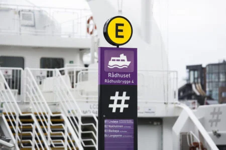 En lila Rådhuset-vägvisningspylon med en gul E-markering bredvid en färja.