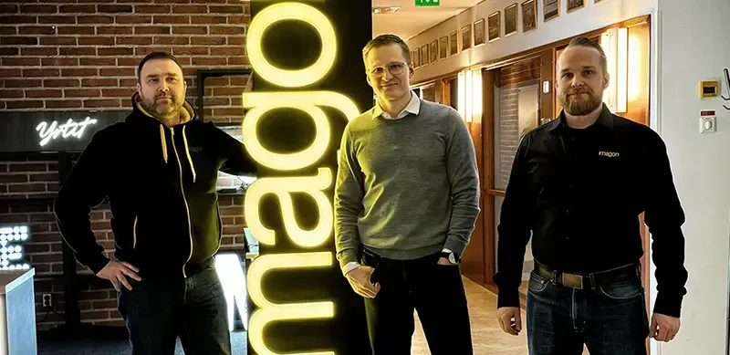 Three people standing around a vertical yellow illuminated Imagon sign
