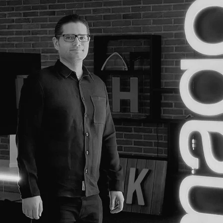 Black-and-white portrait of Tapio Rissanen standing in front of a brick wall and illuminated letters