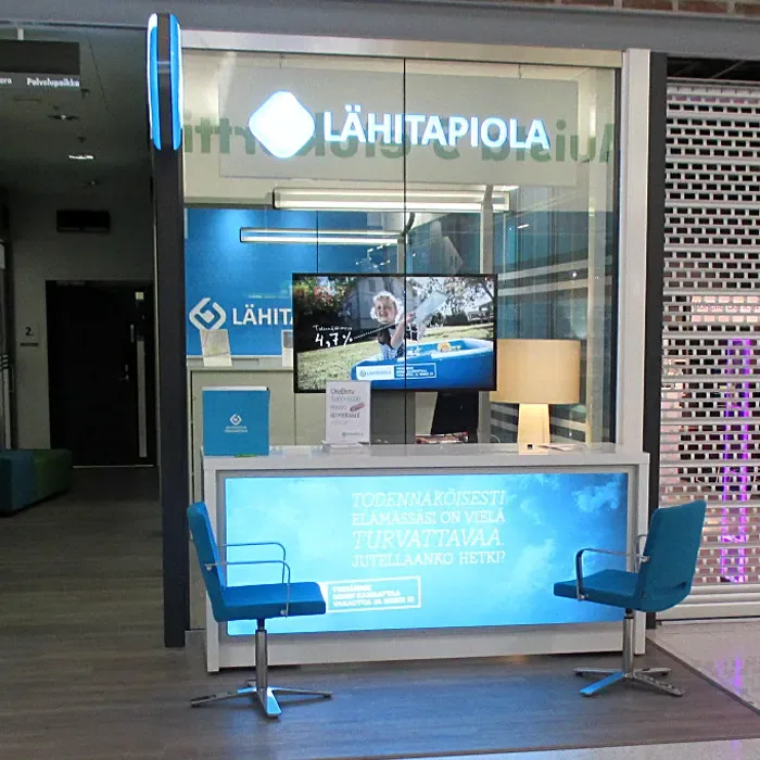 A blue LähiTapiola service counter, two chairs and a digital display.