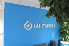A white LähiTapiola logo on a bright blue office wall. A white LähiTapiola logo on a bright blue office wall.