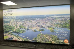 A large illuminated wall advertisement with an aerial city view and the OP logo. A large illuminated wall advertisement with an aerial city view and the OP logo.