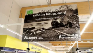 A large welcome sign for S-Market Uitto featuring a black-and-white lakeside scene. A large welcome sign for S-Market Uitto featuring a black-and-white lakeside scene.