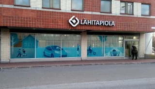 A white LähiTapiola facade sign and blue window graphics on a brick building. A white LähiTapiola facade sign and blue window graphics on a brick building.
