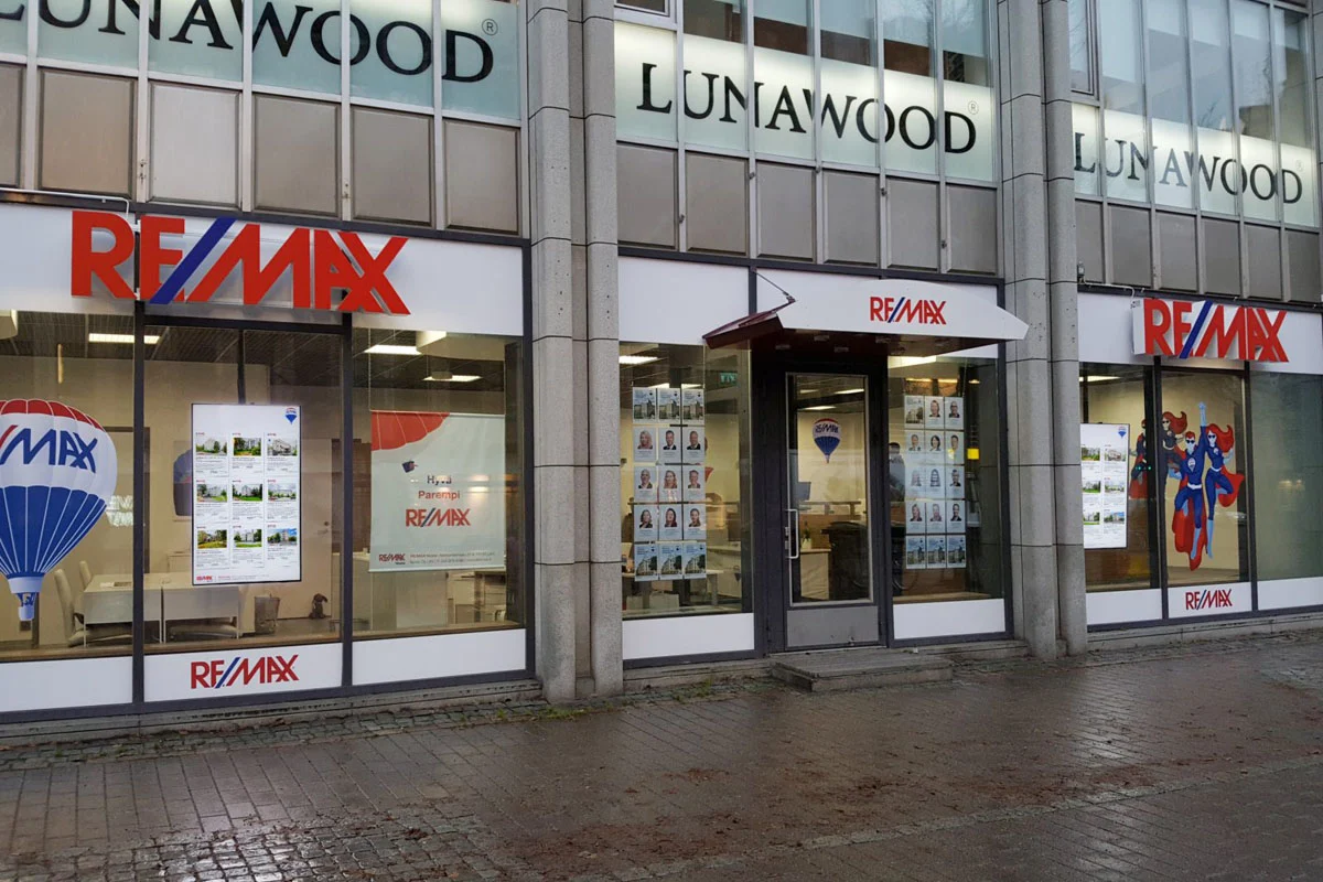 RE/MAX-toimiston näyteikkunat asuntoilmoituksineen ja punaiset julkisivutunnukset.