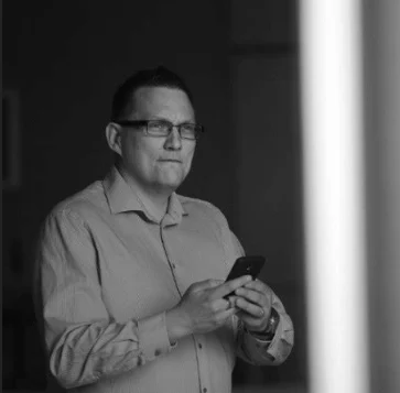 Black-and-white portrait of Marko Kolehmainen standing with a phone in his hands