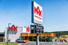 A tall MAX advertising pylon and restaurant facade signs near the drive-in entrance.