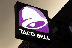 A projecting Taco Bell illuminated sign with a purple bell logo and white lettering.