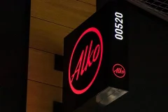 A projecting black illuminated sign with a red Alko logo and the white number 00520.