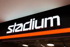 White illuminated Stadium lettering on a black background above an orange stripe.