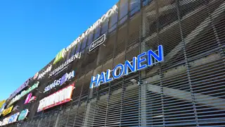 Blue Halonen sign and other shop signs on a shopping centre's louvred facade