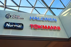 Clas Ohlson, Halonen, Normal and Tokmanni signs on a shopping centre wall beneath a glass roof