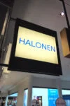 Halosen riippuva valokyltti Halosen neliönmuotoinen valokyltti mustassa kehyksessä kauppakeskuksen käytävällä