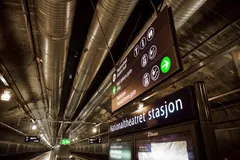 A Nationaltheatret stasjon sign and illuminated direction arrows in a tunnel-like passage.