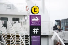 A purple Rådhuset pier sign and yellow E marker beside a ferry.