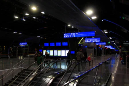 Blue timetable displays and yellow direction signs in a dim station concourse. Blue timetable displays and yellow direction signs in a dim station concourse.
