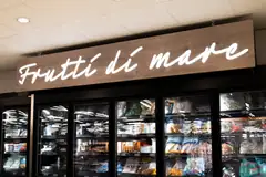 Valkoinen Frutti di mare -valoteksti puukuvioisessa opasteessa pakastekaappien yläpuolella Prisma Sellossa