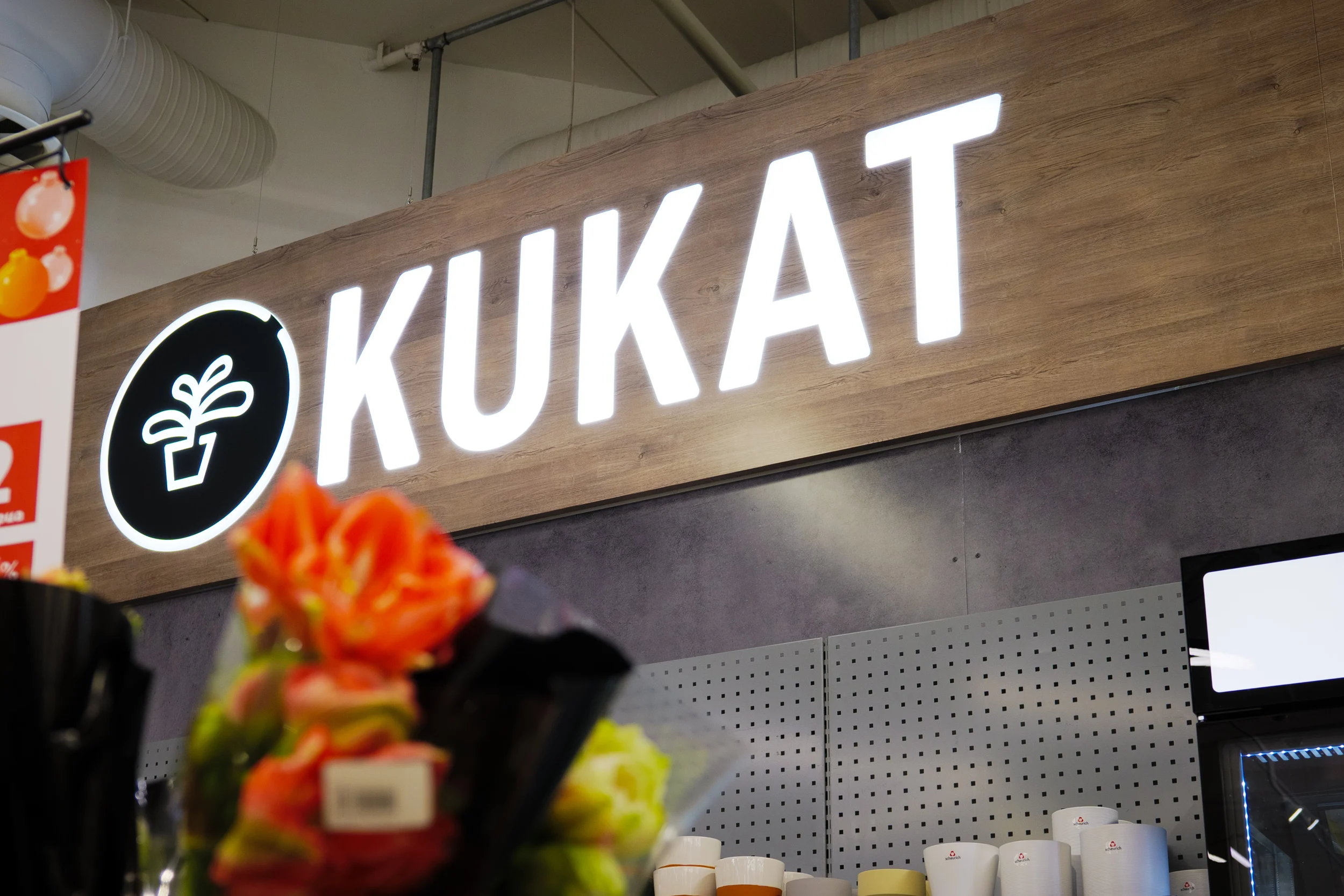 Valaistu Kukat-teksti ja kukkaruukkusymboli puukuvioisessa opasteessa Prisma Sellossa