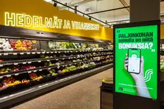 Illuminated lettering above a fruit and vegetable section and a green advertising display in a grocery store.