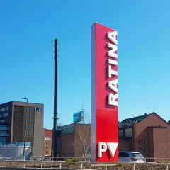 En hög röd Ratina-pylon vid en gata mot blå himmel.