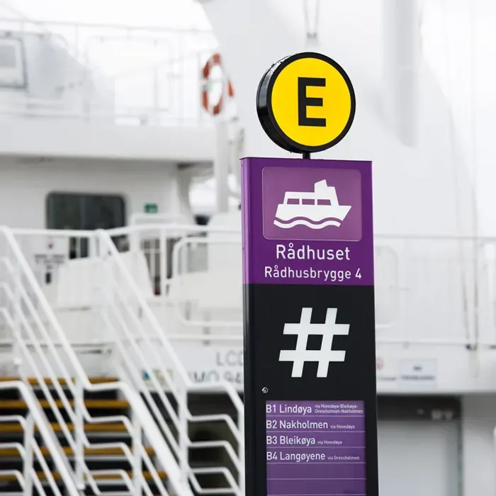 A purple Rådhuset signpost with a yellow E marker and a ferry behind it.