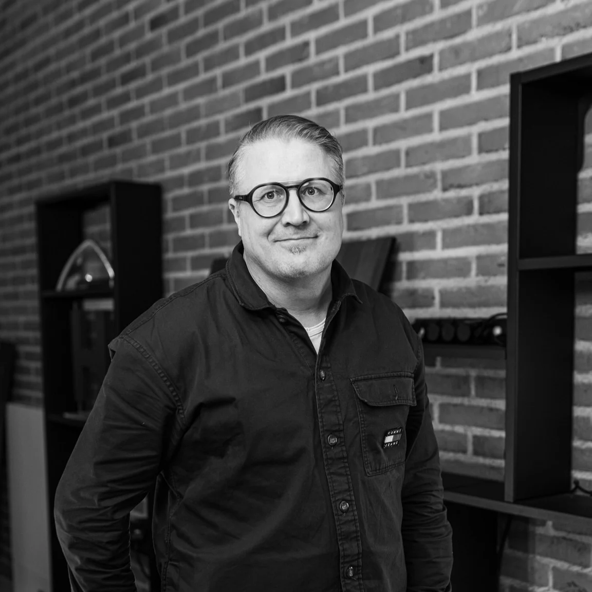 Black-and-white portrait of Jari Partanen standing in front of a brick wall