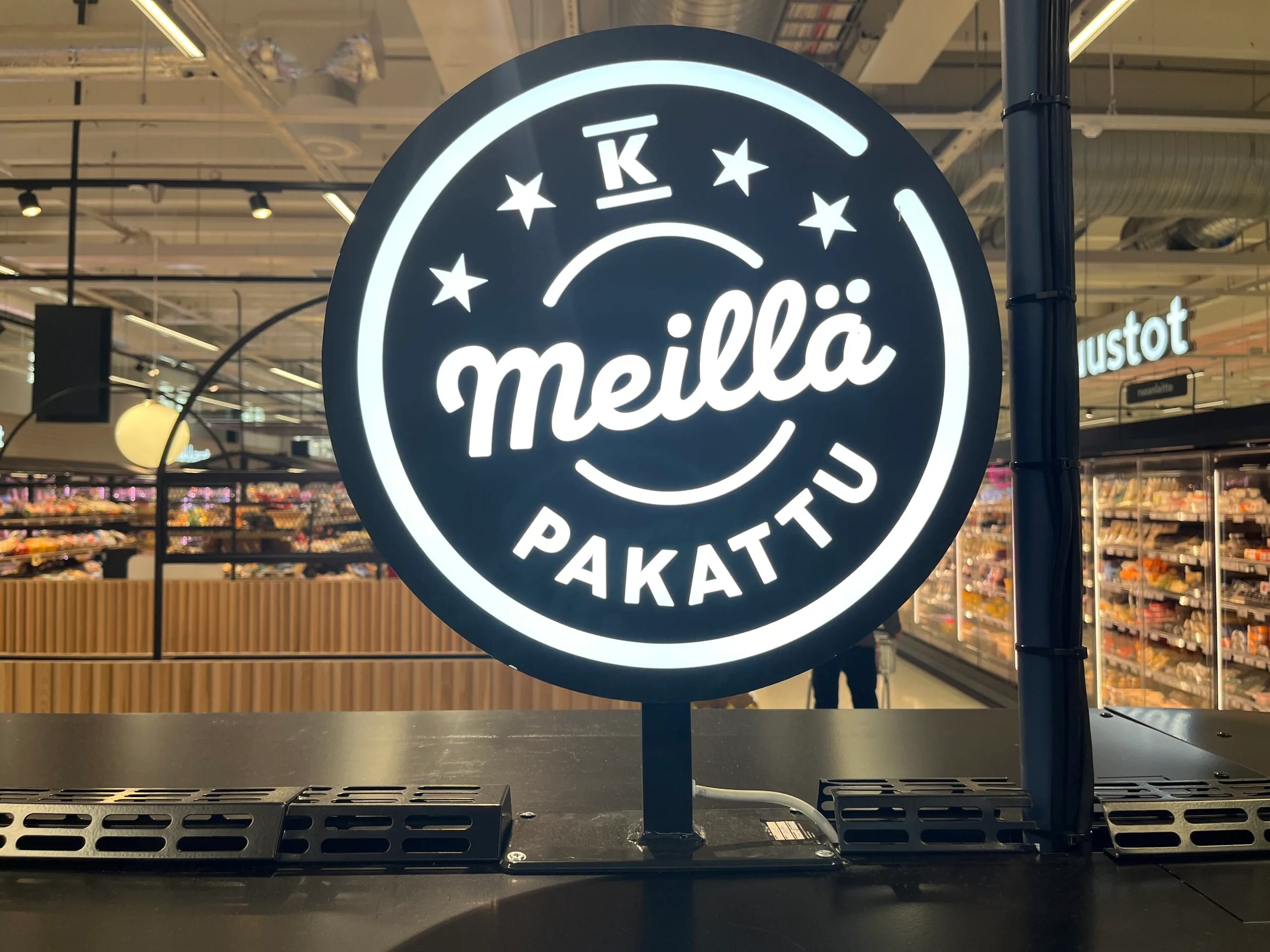 Pyöreä mustavalkoinen Meillä pakattu -valokyltti K-tunnuksella