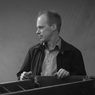 Janne Rissanen beside a metal frame in a production workshop, shown in black and white.