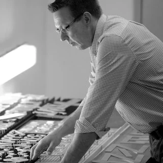 Jarmo Raitanen working on parts laid out on a table in a black-and-white photograph.