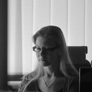 Kati Eronen wearing glasses and sitting in an office, shown in black and white.