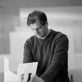 Pertti Vesala examining white parts on a workbench in a black-and-white photograph.