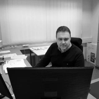 Samuli sitting behind a computer monitor in an office, shown in black and white.