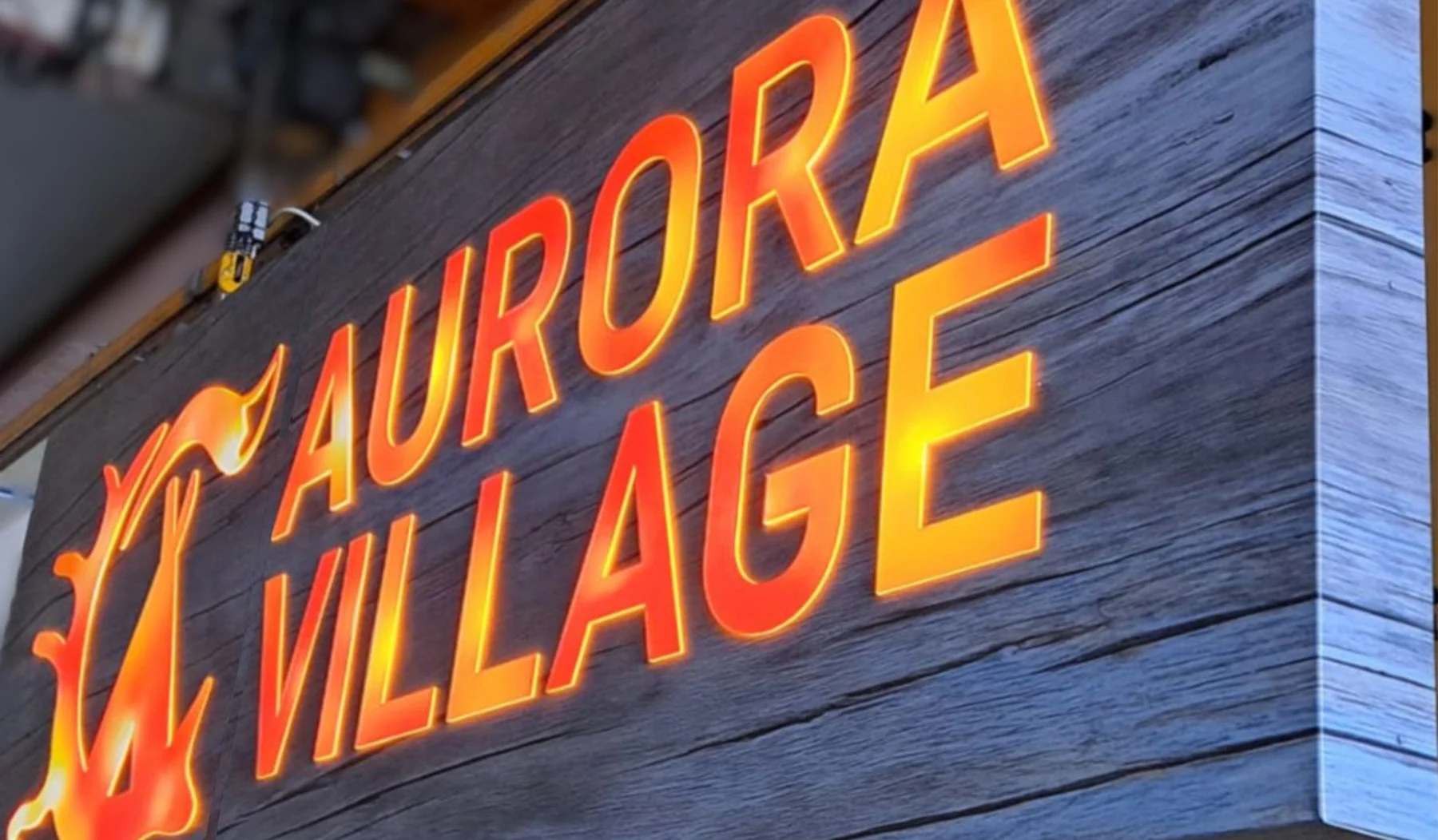Aurora Village -valokirjaimet oranssina puukuvioisella taustalla