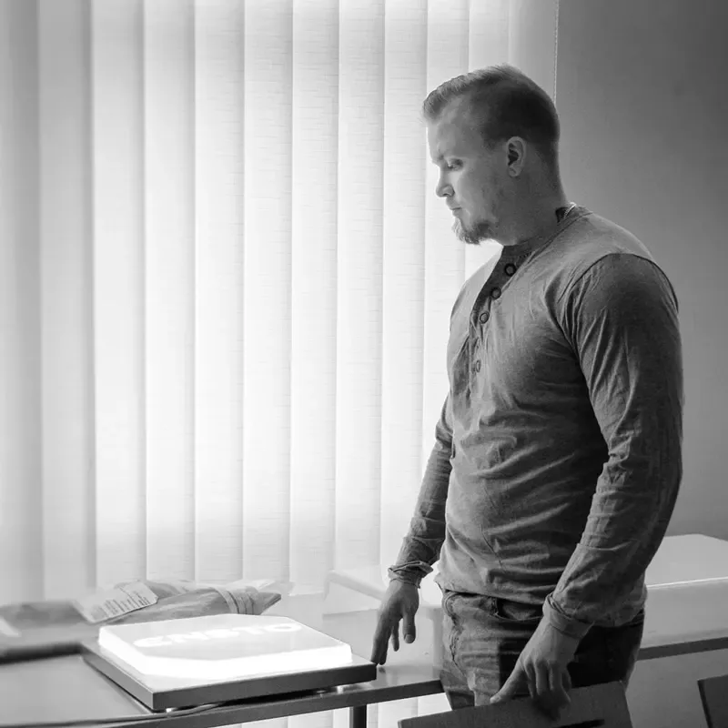 Timo Juntunen standing beside a desk and window in a black-and-white photograph.